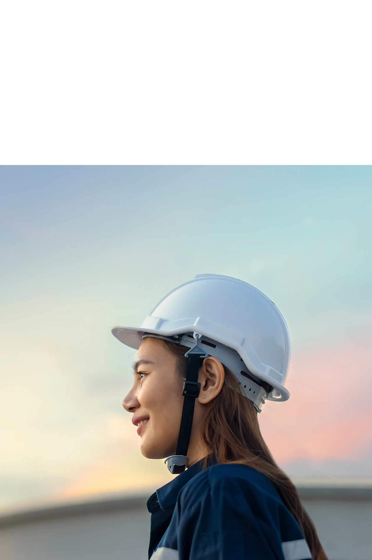 Woman wearing a hardhat outside, taking notes while looking at the sunset