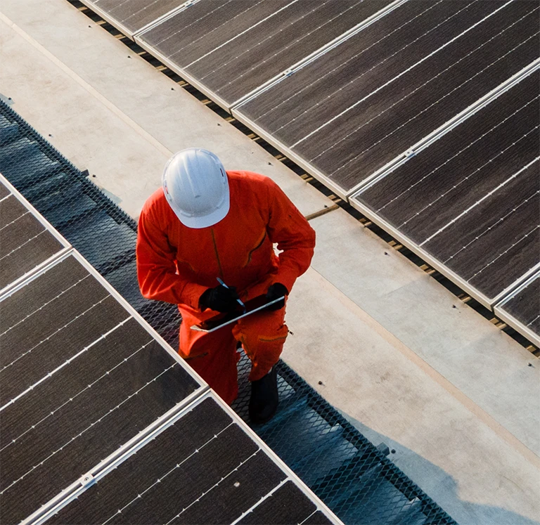 Top view of worker wearing hardhat inspecting rows of solar panels
